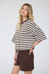 A woman with long blonde hair wears the Stephanie Striped Cardigan paired with brown shorts. She stands facing forward with one hand in her pocket against a plain light background.
