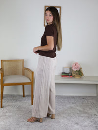A woman wearing a brown t-shirt and Louise Linen Blend Pant featuring wide-leg trousers with a subtle vertical stripe pattern and an elastic waist.