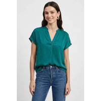 A woman wears a Naked Zebra - Drop Shoulder Regular Blouse in teal woven polyester with a V-neckline, paired with blue jeans.