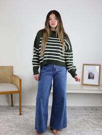 A person wearing a forest green and white striped Noa Striped Sweater in an oversized cotton knit paired with wide-leg blue jeans.