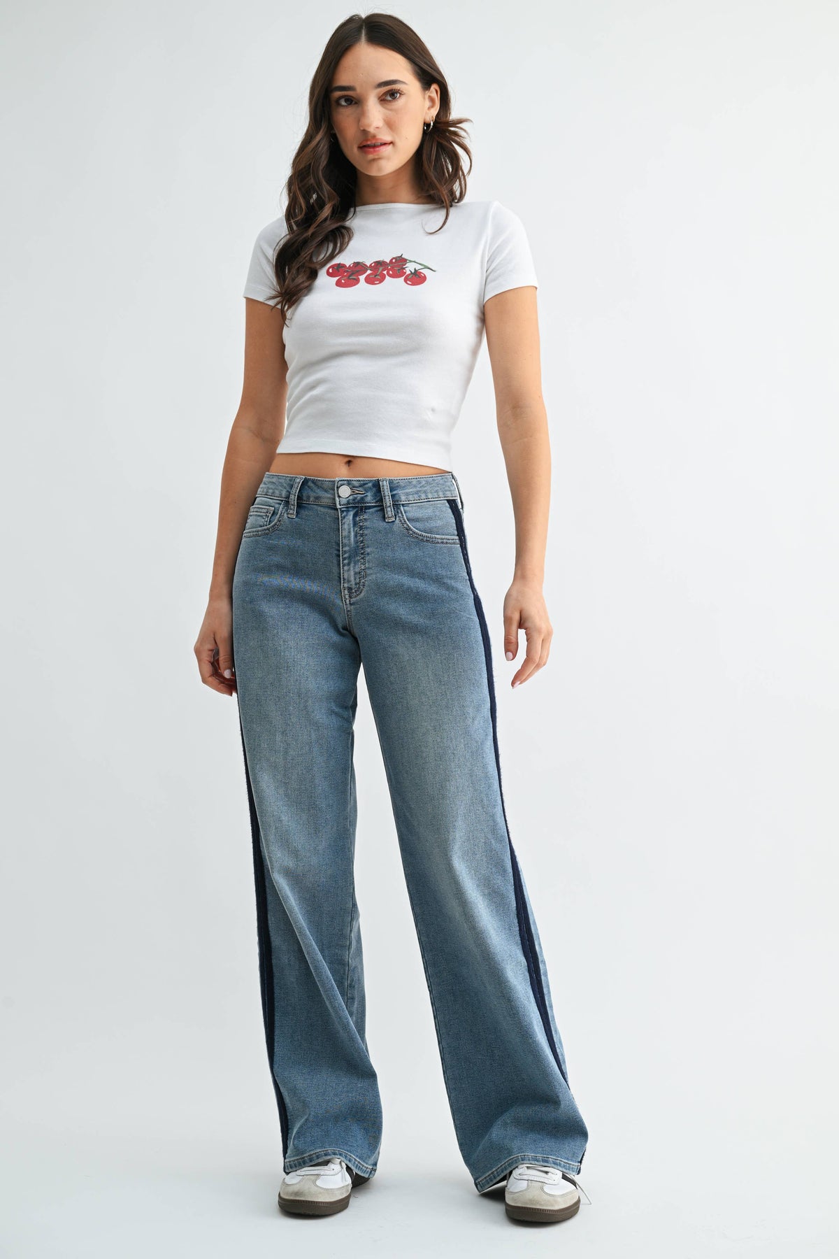 A woman wearing a white crop top with red prints and JBD - Mid Rise Sleek Tuxedo Sweat Pants in medium denim (DP914: 24) stands against a plain white background.