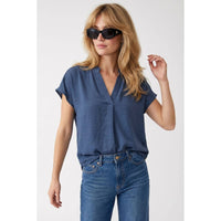 A woman wearing a Naked Zebra - Drop Shoulder Regular Blouse: Chocolate / L in a blue drop shoulder woven polyester v-neck style with blue jeans.