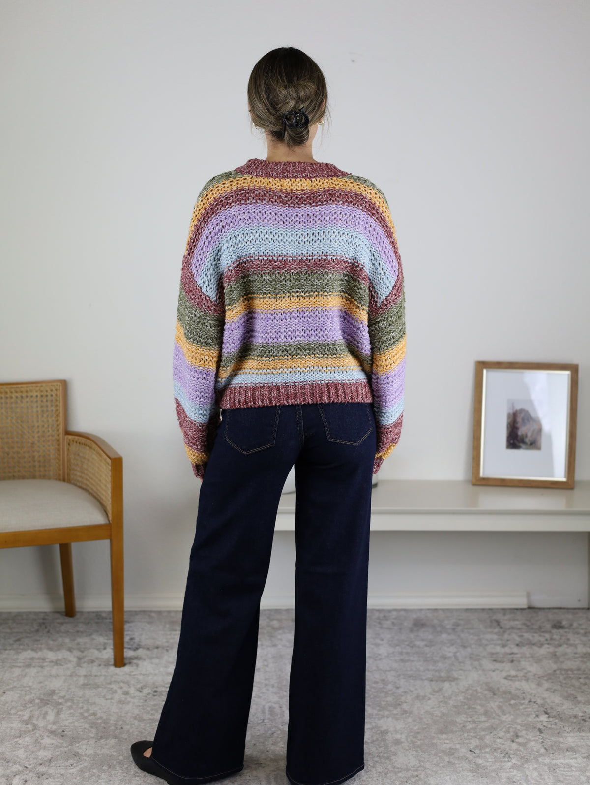 A person seen from behind wearing a cozy, multi-colored striped Reign Striped Knit Sweater and dark blue wide-leg jeans.