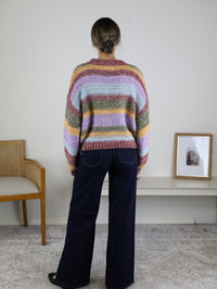 A person seen from behind wearing a cozy, multi-colored striped Reign Striped Knit Sweater and dark blue wide-leg jeans.