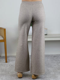 A person wearing the Rebecca Sweater/Pant Set, featuring high-waisted, wide-leg beige knit trousers paired with beige low-heeled shoes.