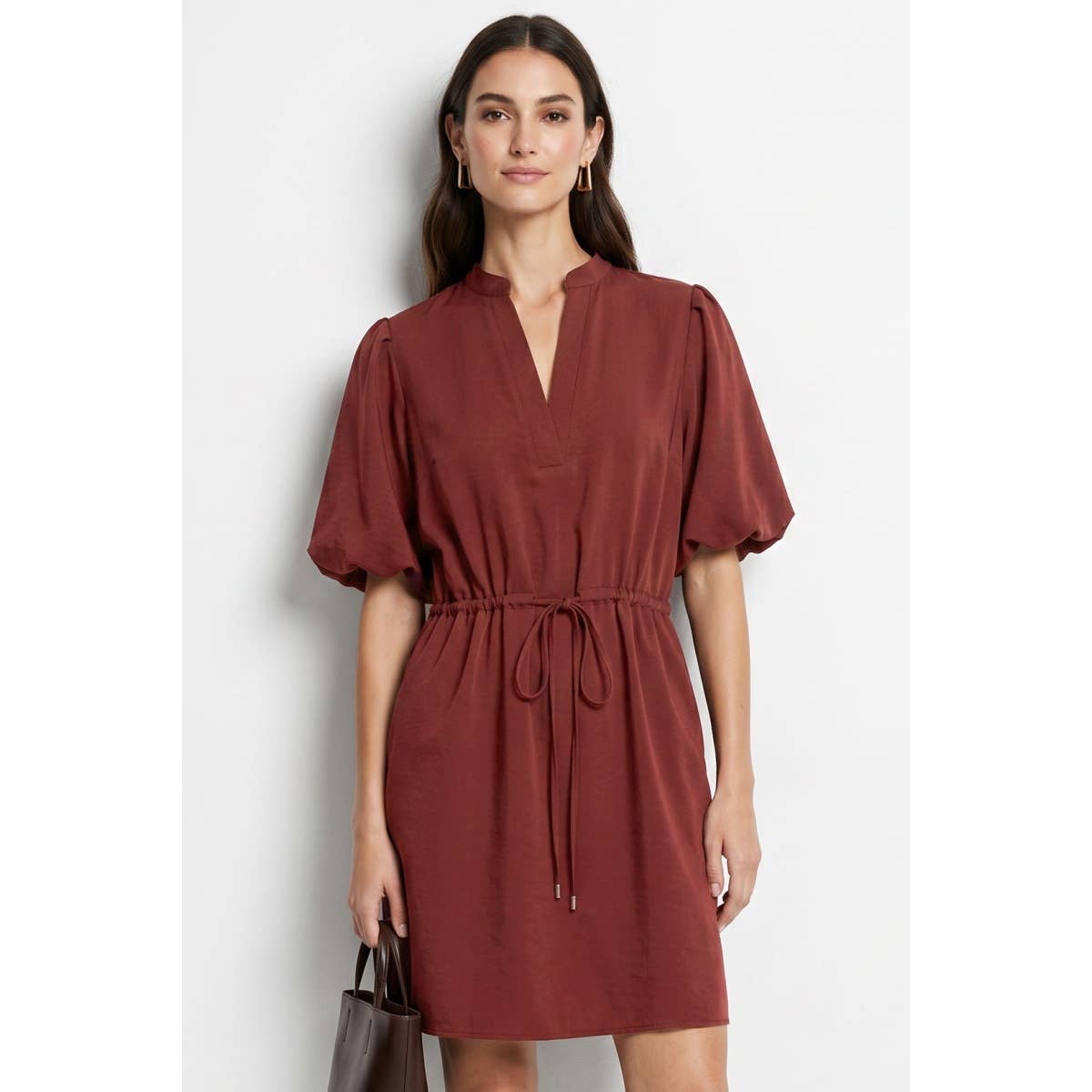 A woman wears a Naked Zebra - Puff Sleeve Cinched Waist Mini Dress: Navy / L in a rust-colored puff sleeve mini dress with a notched neckline and a cinched, drawstring waist.