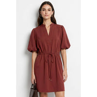 A woman wears a Naked Zebra - Puff Sleeve Cinched Waist Mini Dress: Navy / L in a rust-colored puff sleeve mini dress with a notched neckline and a cinched, drawstring waist.
