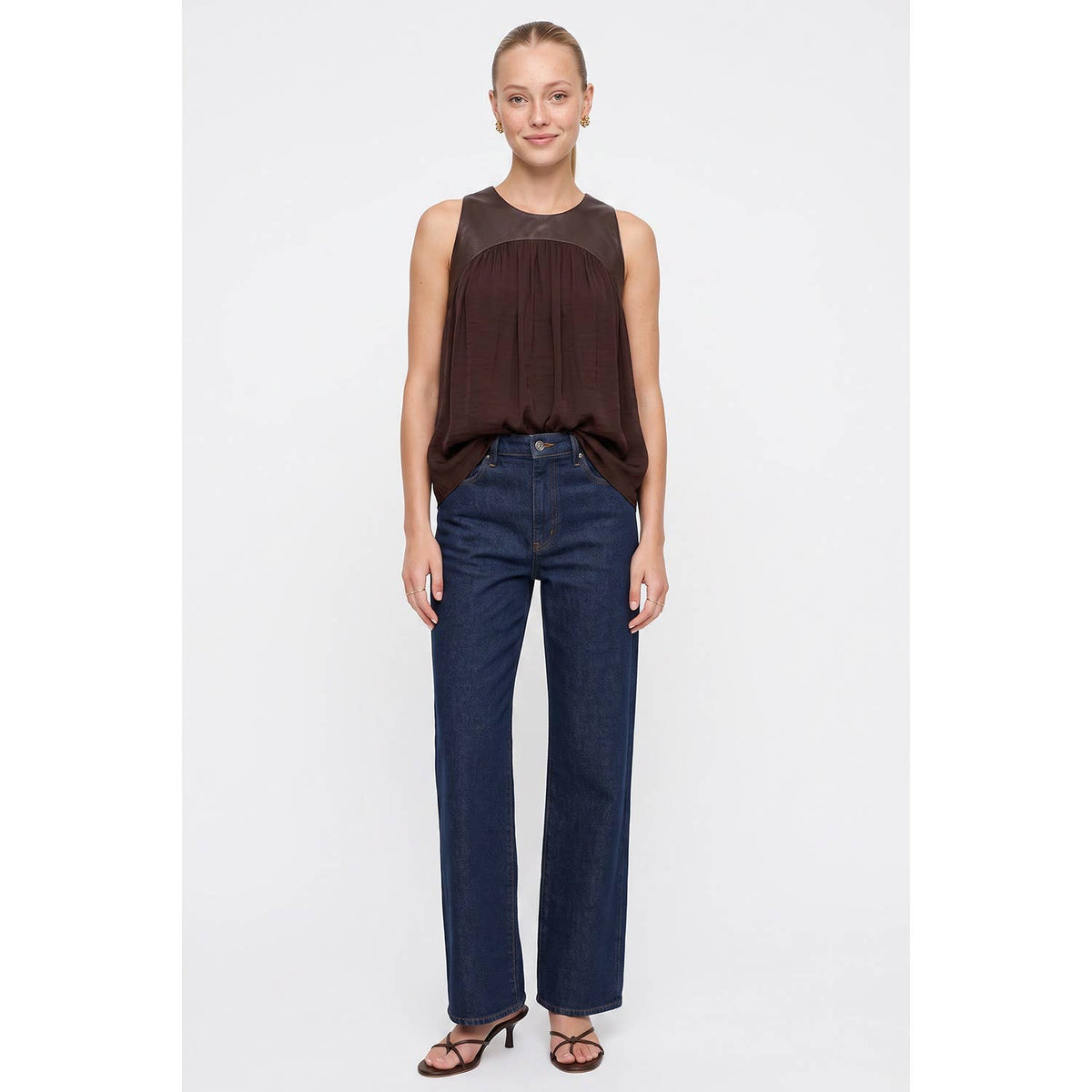 A person wearing a Naked Zebra - Vegan Leather Yoke Satin Tank: Wine / L with a dark brown mixed-media vegan leather top and straight-leg dark wash jeans.