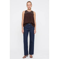 A person wearing a Naked Zebra - Vegan Leather Yoke Satin Tank: Wine / L with a dark brown mixed-media vegan leather top and straight-leg dark wash jeans.
