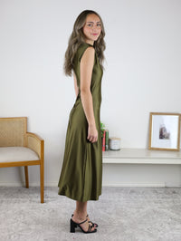 A woman in profile wears a sleeveless olive green Desi Drape Neckline Maxi Dress with a draped neckline and black heeled sandals.