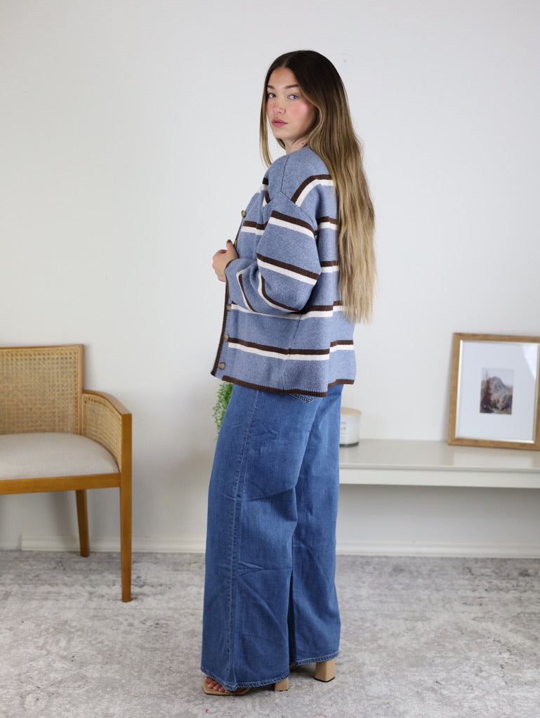 A person wearing a blue, white, and brown Nora Stripe Button Down Knit Cardigan and wide-leg blue jeans.