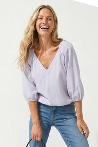 A smiling woman wearing a Naked Zebra - Elastic Puff Sleeve V-neck Blouse: Burgundy / L, featuring a V-neck and light purple puff sleeves.