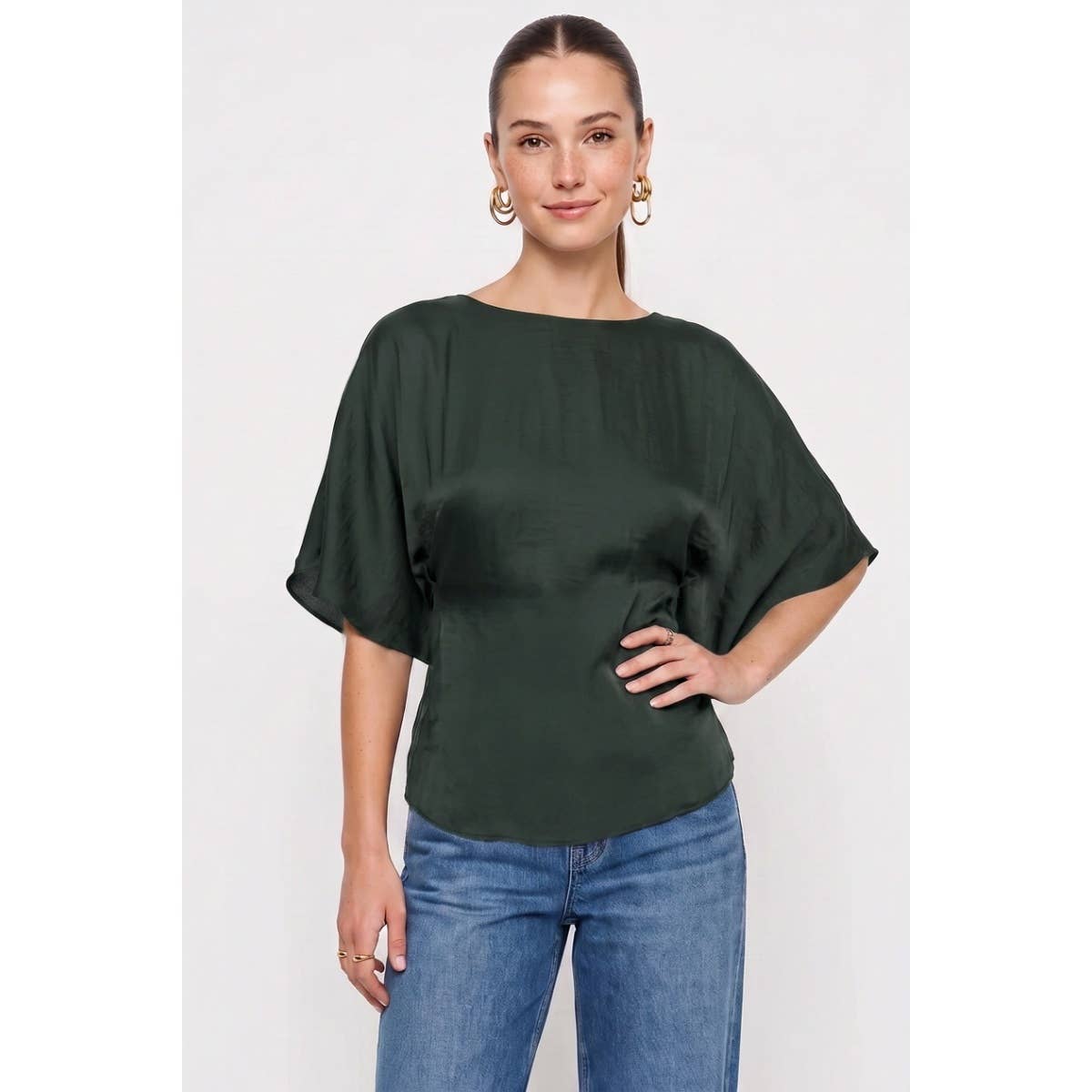 A dark green, short-sleeved dolman blouse with a boat neckline from the Naked Zebra - Back Tie Dolman Sleeve Silky Fall Blouse collection, worn with blue jeans.