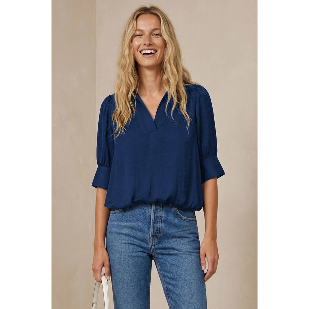 A smiling woman wears a navy blue, half-sleeve Naked Zebra - Half Sleeve Hi-lo Bubble Hem Blouse: Wine / L with a v-neck, paired with blue jeans.