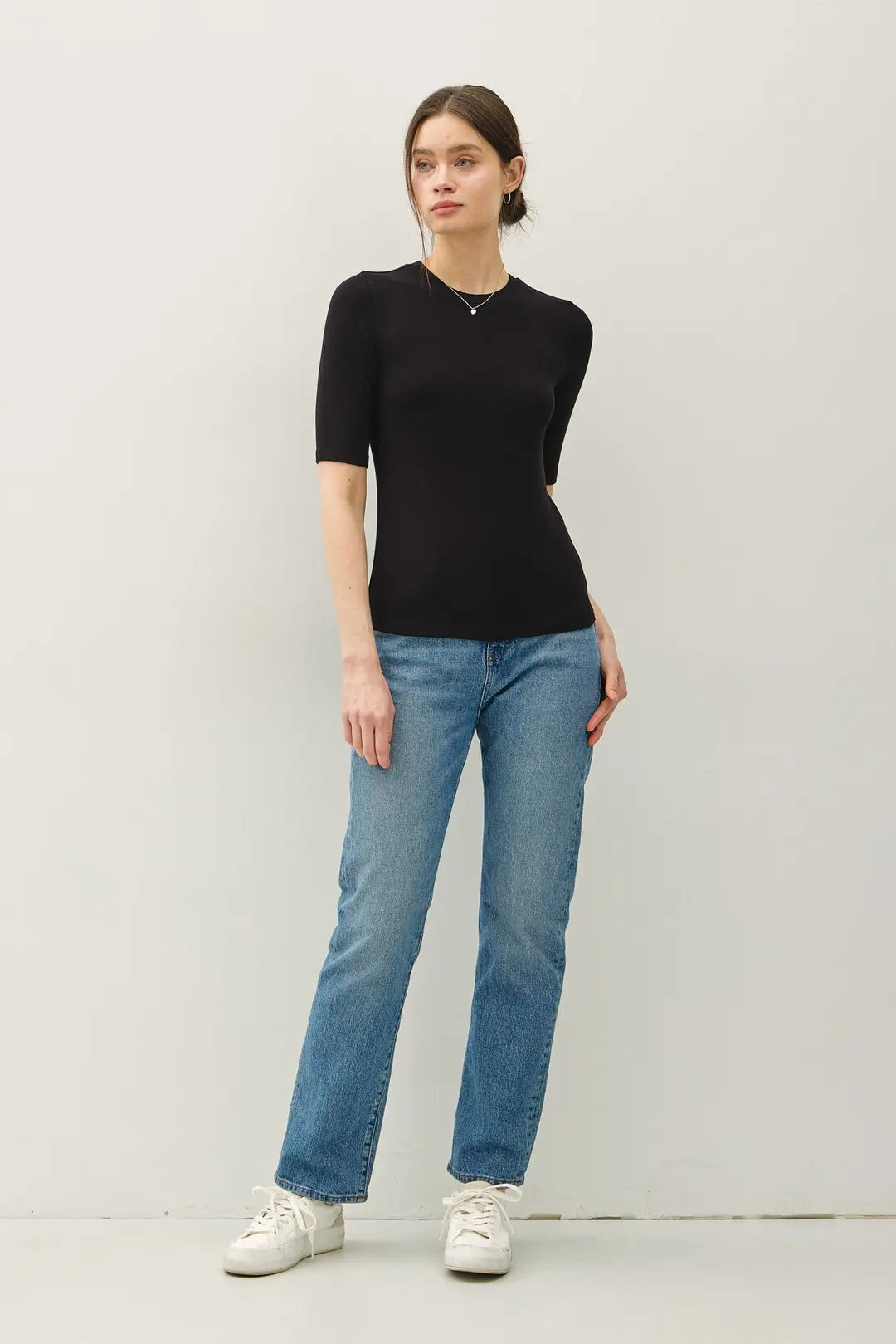 A woman wearing a black, fitted Crew Short Sleeve Top, blue jeans, and white sneakers.