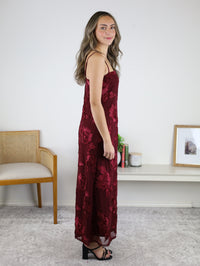 A woman wearing an Axel Applique Mesh Maxi Dress, a sleeveless, ankle-length maroon mesh gown with romantic floral applique and black heeled sandals.