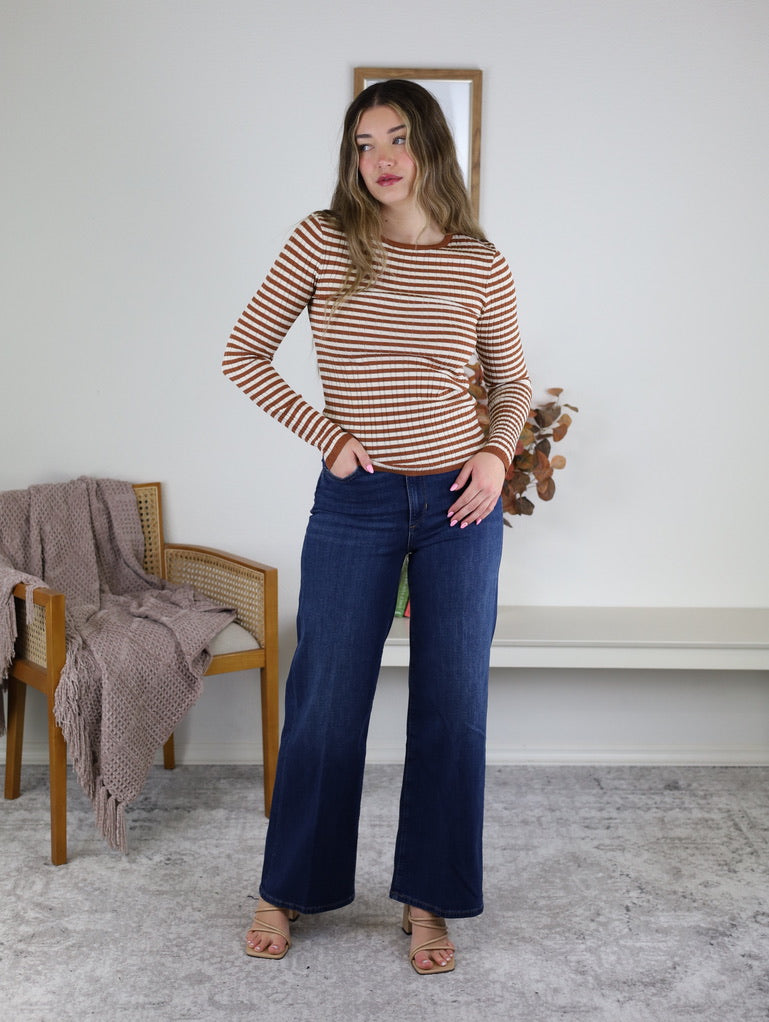 A woman wears a Mindy Ribbed Striped Top in terracotta stripes paired with dark blue wide-leg jeans.