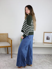 A person wearing an oversized forest green and white striped Noa Striped Sweater with wide-leg blue jeans.