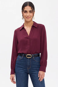 A woman wearing a Naked Zebra - Neck Shirt With Open Seam Sleeve: Wine / L paired with dark blue jeans and a black belt.