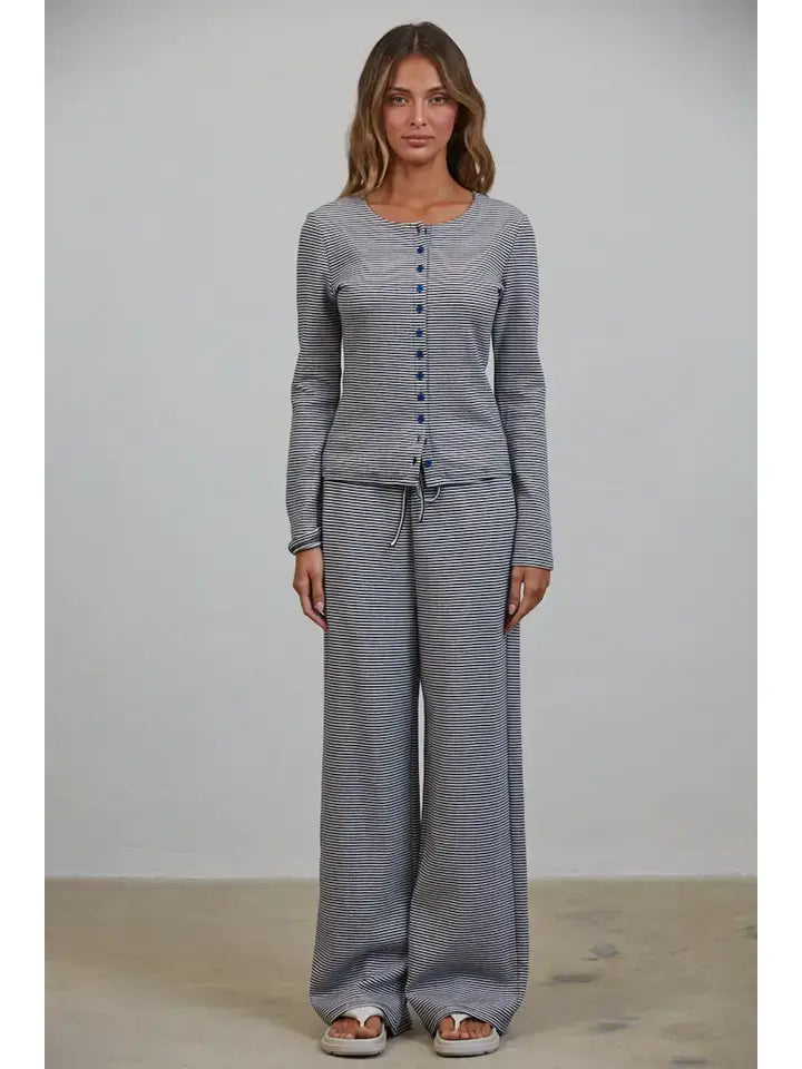 A woman stands against a plain background wearing the Creamon - CTP3592 BROWN Lounge Striped Button Down Top & Pants Set in brown stripe, paired with white sandals.