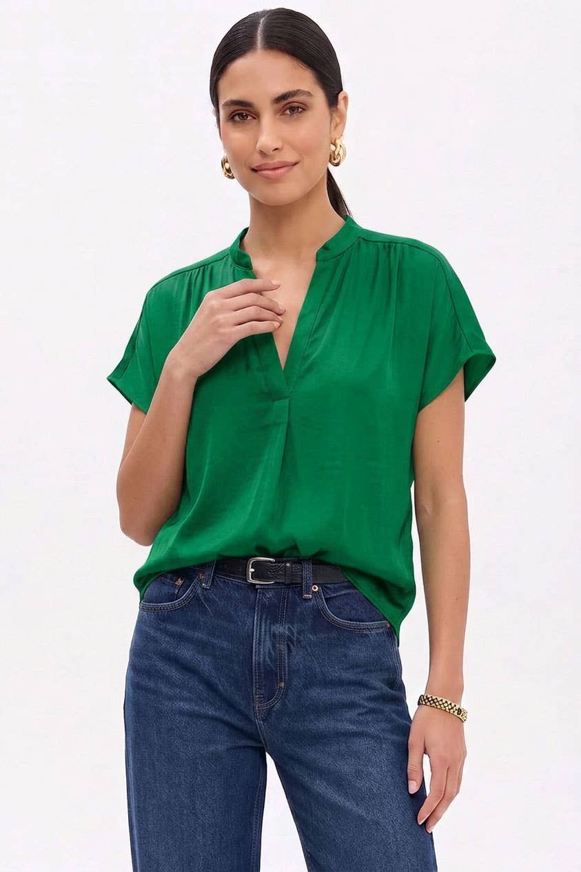 A woman wears a Naked Zebra - Drop Shoulder Regular Blouse: Chocolate / L, featuring a green regular drop shoulder design with a split V-neckline, tucked into dark blue jeans with a black belt.