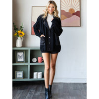 A woman stands indoors wearing the Veveret - Knit Body Denim Layerd Jacket: Cream / Denim / L over a white turtleneck, black skirt, and ankle boots, posing with one hand in her pocket in front of bookshelves and flowers.