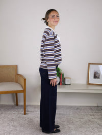 A woman wears a Striped Rugby Top with Contrast Collar, featuring long sleeves and horizontal stripes, paired with dark blue wide-leg jeans.