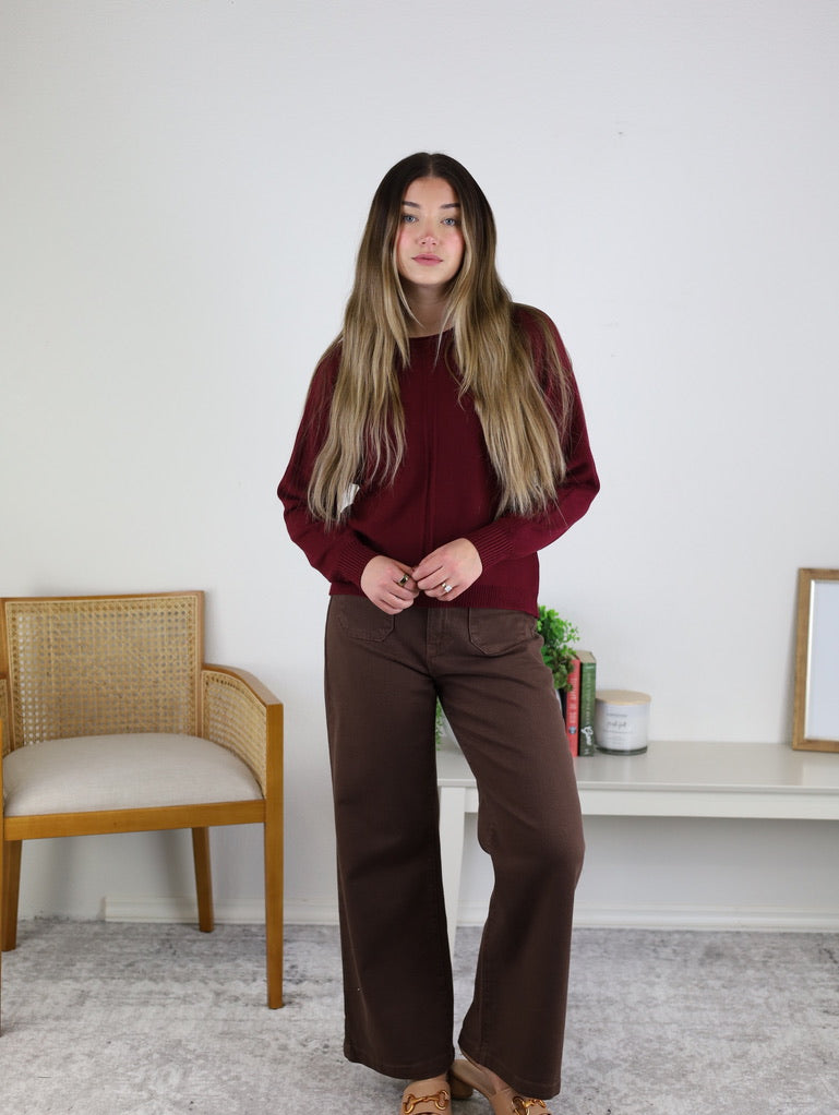 A person wearing an Eli Front Seam Sweater in burgundy with a vertical front seam, paired with brown wide-leg pants.