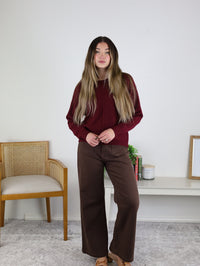 A person wearing an Eli Front Seam Sweater in burgundy with a vertical front seam, paired with brown wide-leg pants.