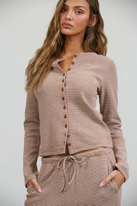 Wearing the Creamon - CTP3592 BROWN Lounge Striped Button Down Top & Pants Set in brown stripe, a woman with long wavy hair poses against a plain background, her hand casually tucked into the pocket of the matching wide leg pants.
