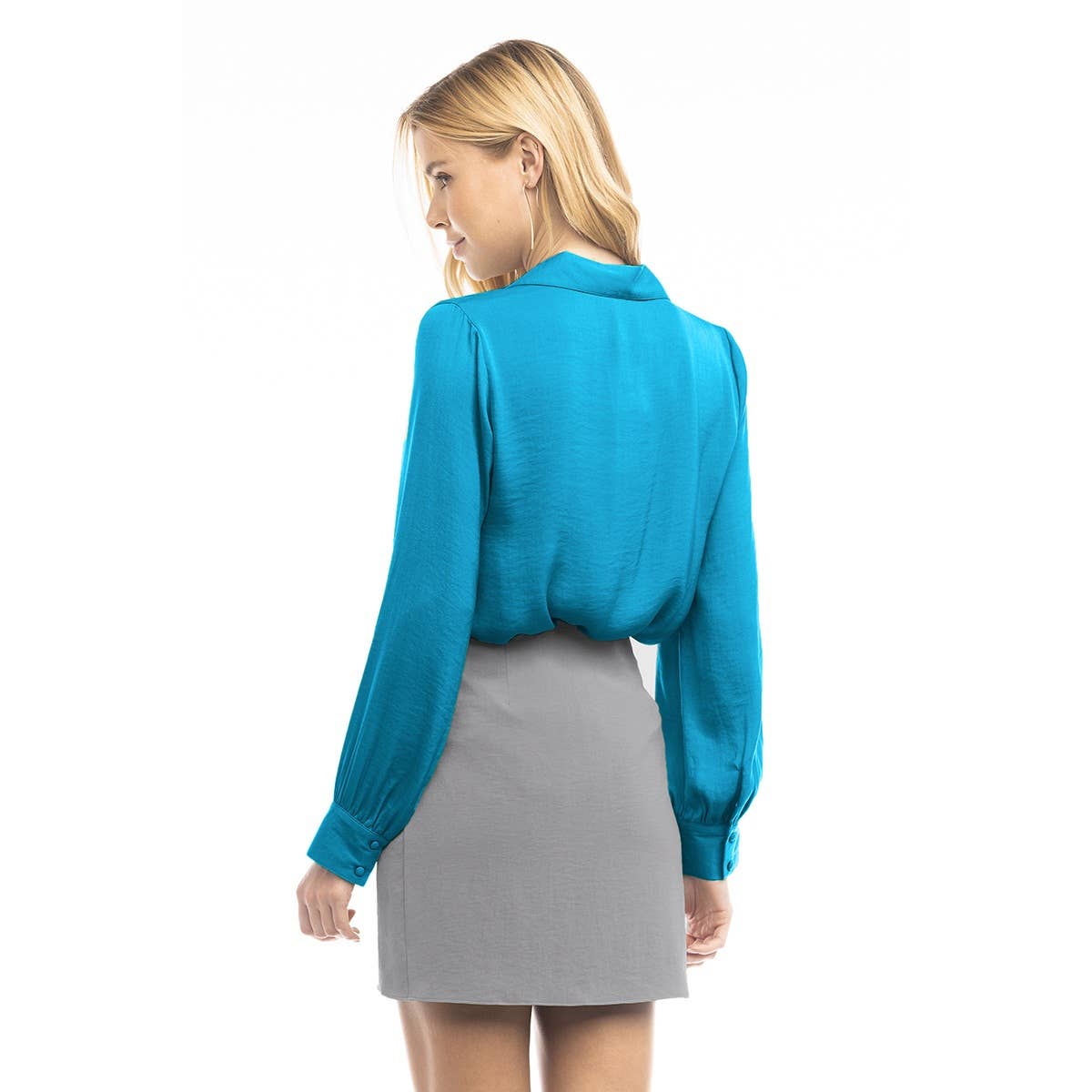 A person wearing a bright blue Naked Zebra - Neck Shirt With Open Seam Sleeve: Wine / L with open sleeve seams tucked into a grey mini skirt.