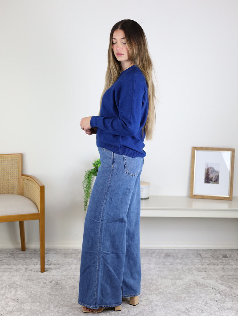 A person wearing a blue Eli Front Seam Sweater with a visible vertical front seam and wide-leg blue jeans.