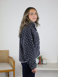 A woman wears a grey, high-pile Reba Fleece Puffer Jacket button-down patterned with small white hearts.