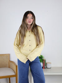 A person wearing a pale yellow, lightweight Jude Raw Edge Cardigan with exposed seam detailing and blue jeans.