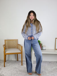 A woman with long hair stands indoors, wearing the Bellamy Textured Striped Crochet Cardigan and wide-leg jeans. She poses beside a wooden chair, with a small table and decor in the background.