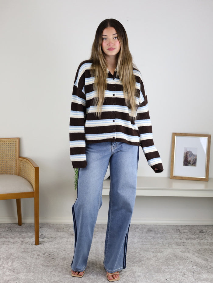 A woman wearing the Remy Multicolor Rolled Neck Knit Cardigan with horizontal stripes in brown, white, and blue, paired with loose-fit blue jeans.