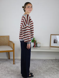 A person wears a cozy, oversized Grayson Relaxed Stripe V-Neck Button Cardigan in red, cream, and gray, paired with dark blue wide-leg jeans and black flats.