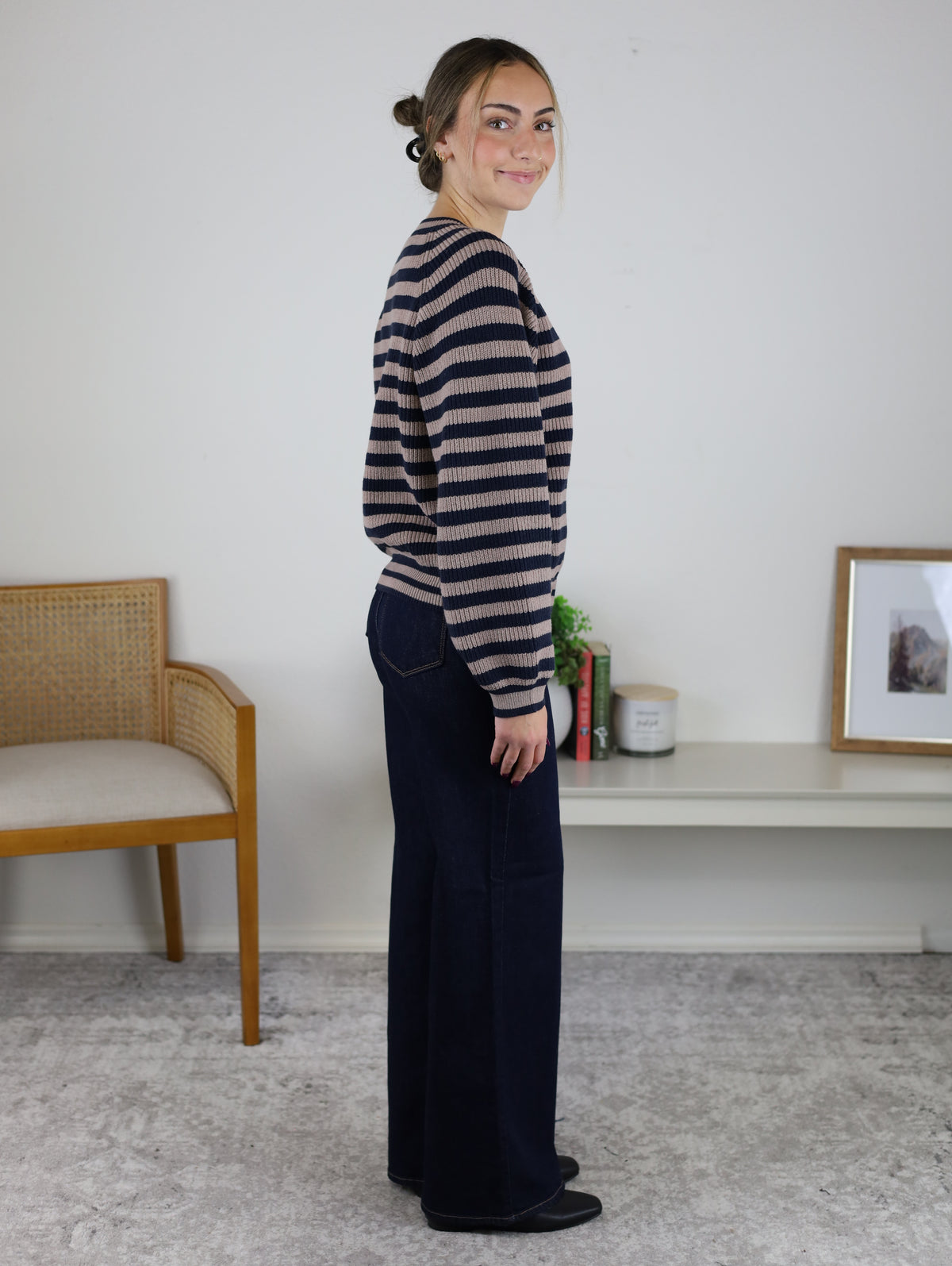 A woman seen from the side wearing a navy and beige Justine Longsleeve Crewneck Striped Sweater and dark wide-leg jeans.