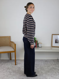 A woman seen from the side wearing a navy and beige Justine Longsleeve Crewneck Striped Sweater and dark wide-leg jeans.