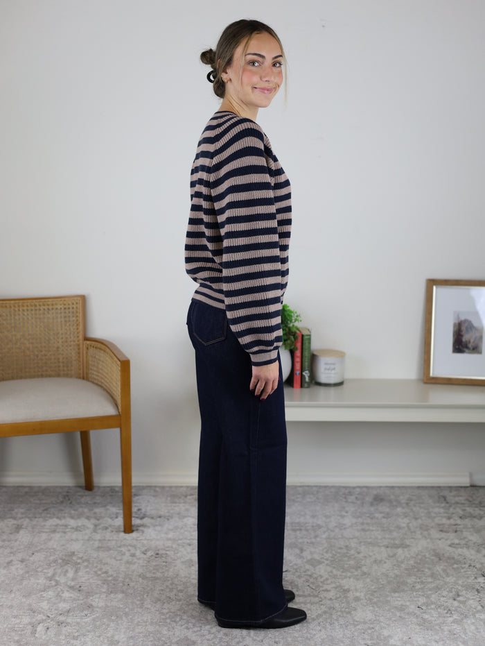 A woman seen from the side wearing a navy and beige Justine Longsleeve Crewneck Striped Sweater and dark wide-leg jeans.
