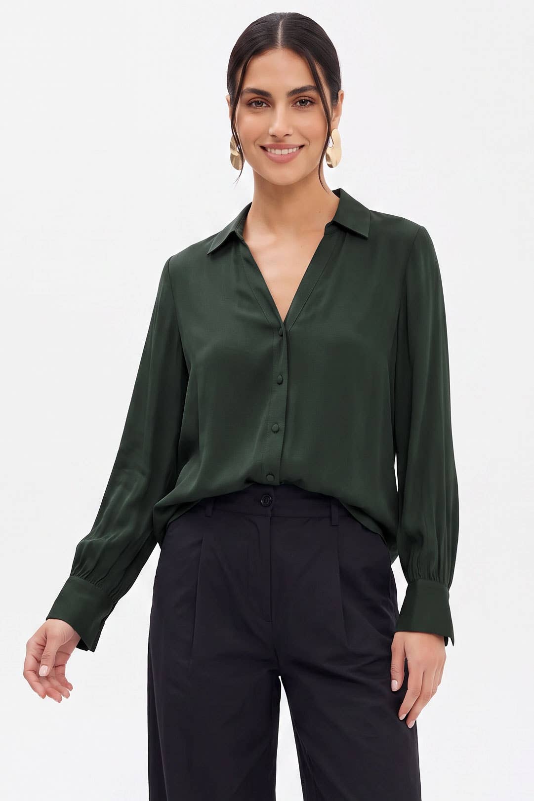 A woman wearing a Naked Zebra - Neck Shirt With Open Seam Sleeve: Black / L in dark green with long sleeves and black trousers.