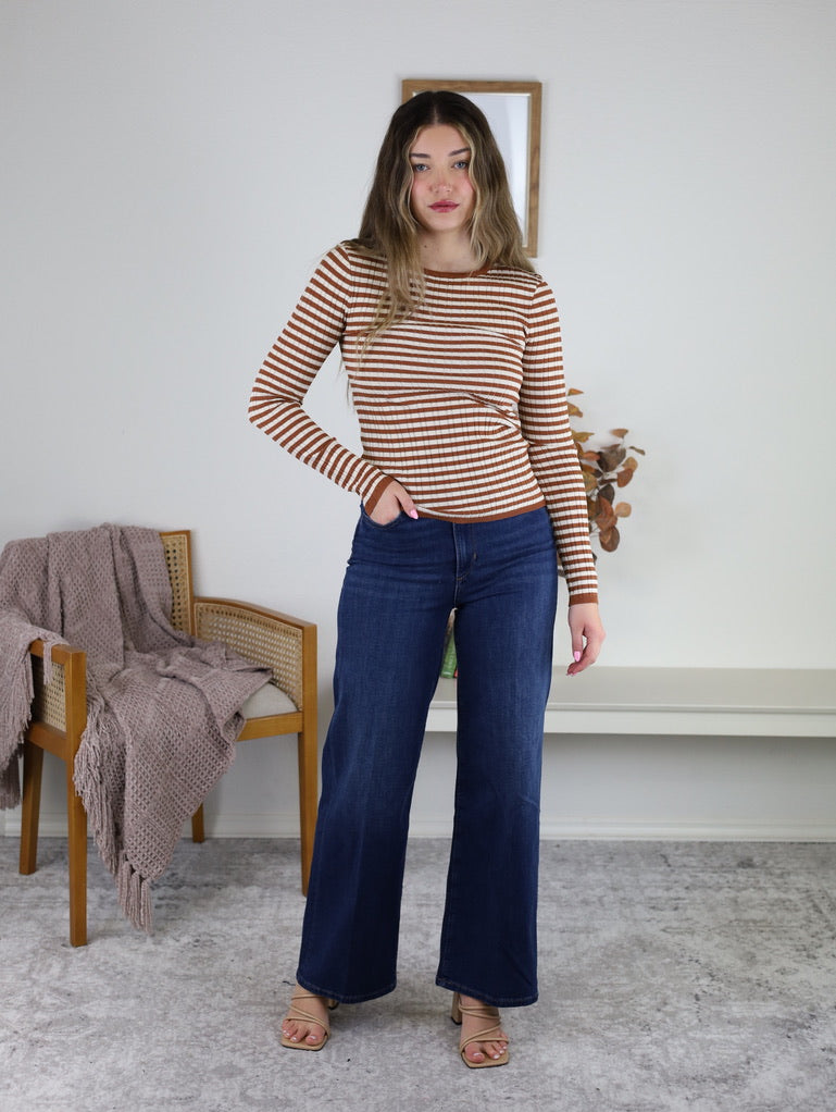 Woman wearing a Mindy Ribbed Striped Top in terracotta stripes with long sleeves, paired with dark blue wide-leg jeans.