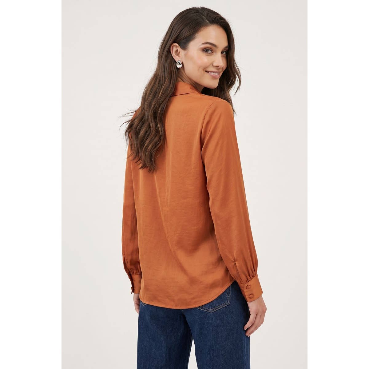 A woman wears a Naked Zebra - Neck Shirt With Open Seam Sleeve: Wine / L, a rust-colored, woven polyester button-up shirt with open-seam sleeves and blue jeans.
