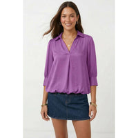 A woman wears a wine Naked Zebra - Half Sleeve Hi-lo Bubble Hem Blouse, featuring a collared V-neck and a hi-lo bubble hem, paired with a dark denim mini skirt.