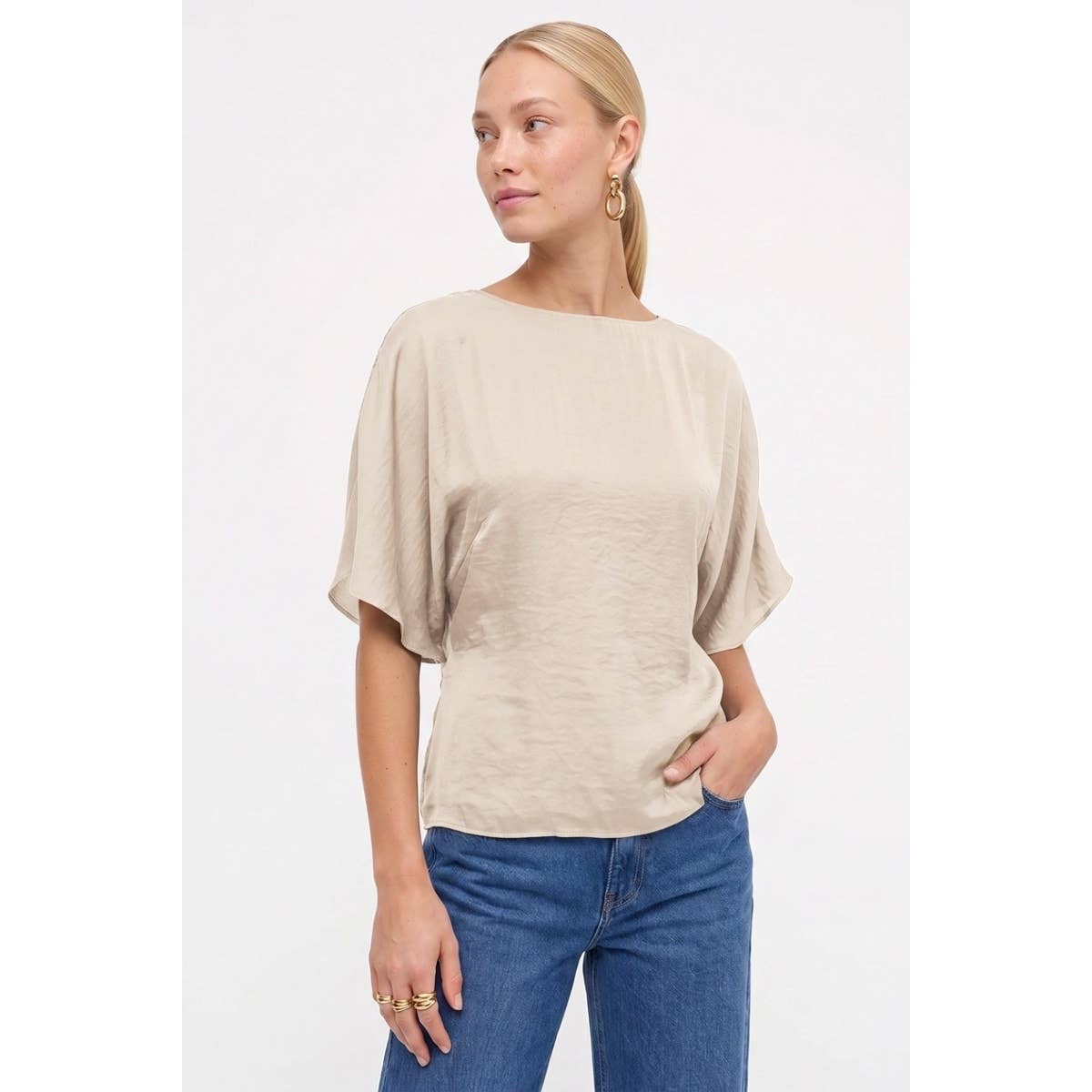 A woman wears a Naked Zebra - Back Tie Dolman Sleeve Silky Fall Blouse in dark navy, styled with a beige, silky dolman sleeve blouse tucked into blue jeans.
