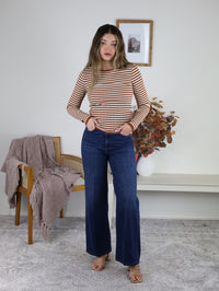 A person wears a Mindy Ribbed Striped Top featuring brown-and-white stripes with solid brown trim at the neckline and cuffs, paired with dark blue wide-leg jeans.