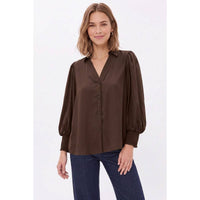 A woman wearing a Naked Zebra - Soft Billowy Sleeve Button Front Blouse: Wine / L with a button front and billowy sleeves, paired with blue jeans.