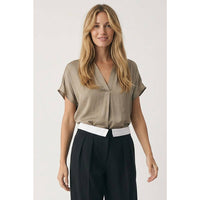 A woman wears a Naked Zebra - Drop Shoulder Regular Blouse: Chocolate / L tucked into black trousers with a prominent white waistband.