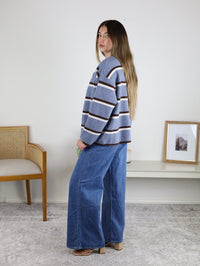 A person wears a blue, white, and brown Nora Stripe Button Down Knit Cardigan with wide-leg blue jeans.