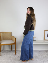 A woman wearing a brown boxy fit Maya Contrast Hem Cardigan with a light green contrast hem and wide-leg blue jeans.